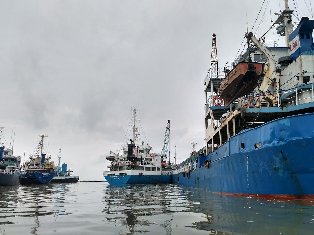 Large blue ships moored at Jakarta harbor under overcast skies, showcasing maritime industry.